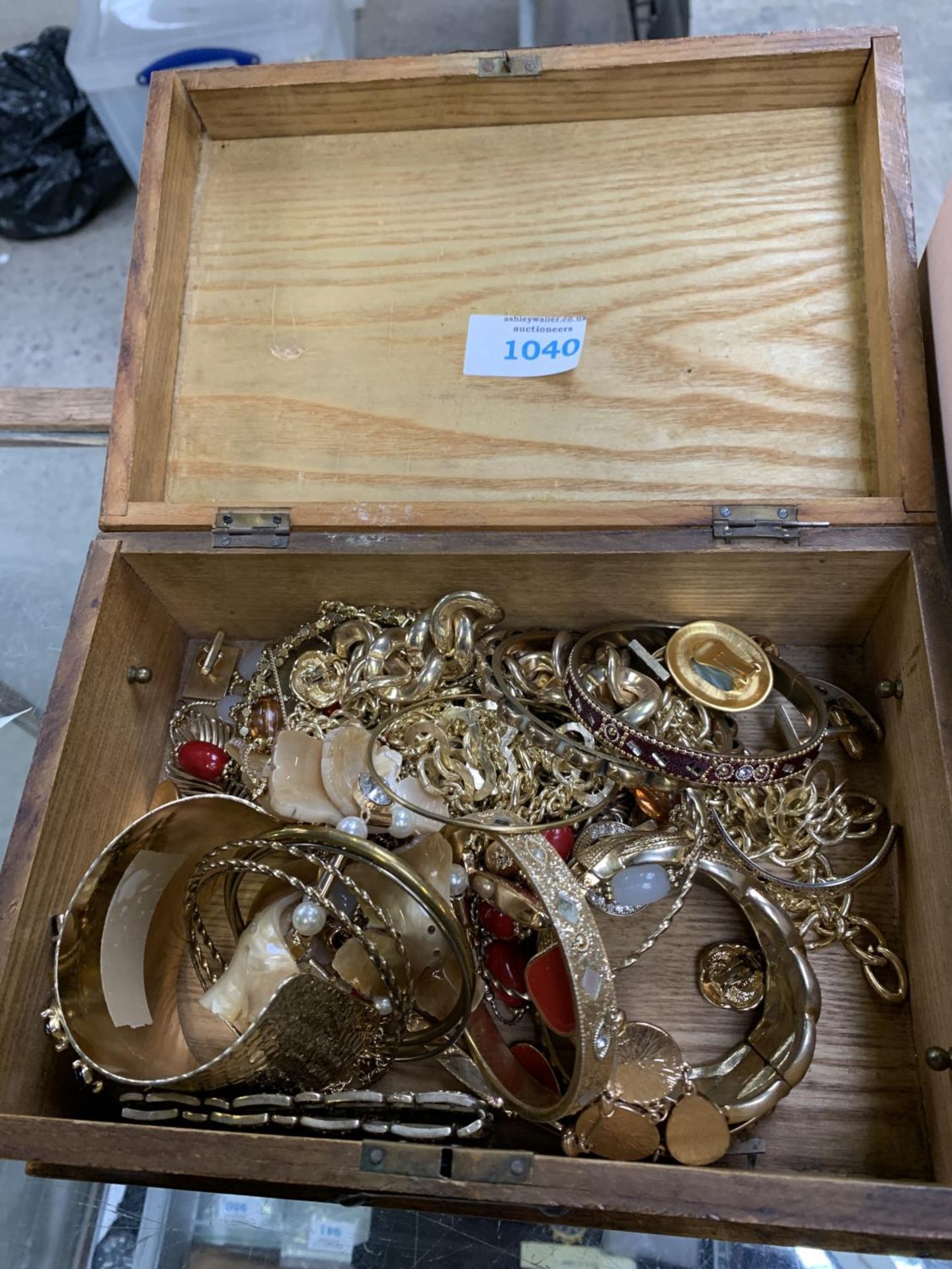 A WOODEN BOX CONTAINING YELLOW METAL COSTUME JEWELLERY