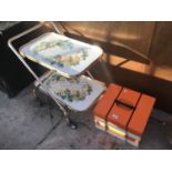 A RETRO FOLDING TEA TROLLEY WITH FLOWER DESIGN AND A STACKING PICNIC CARRIER WITH INDIVIDUAL TRAYS