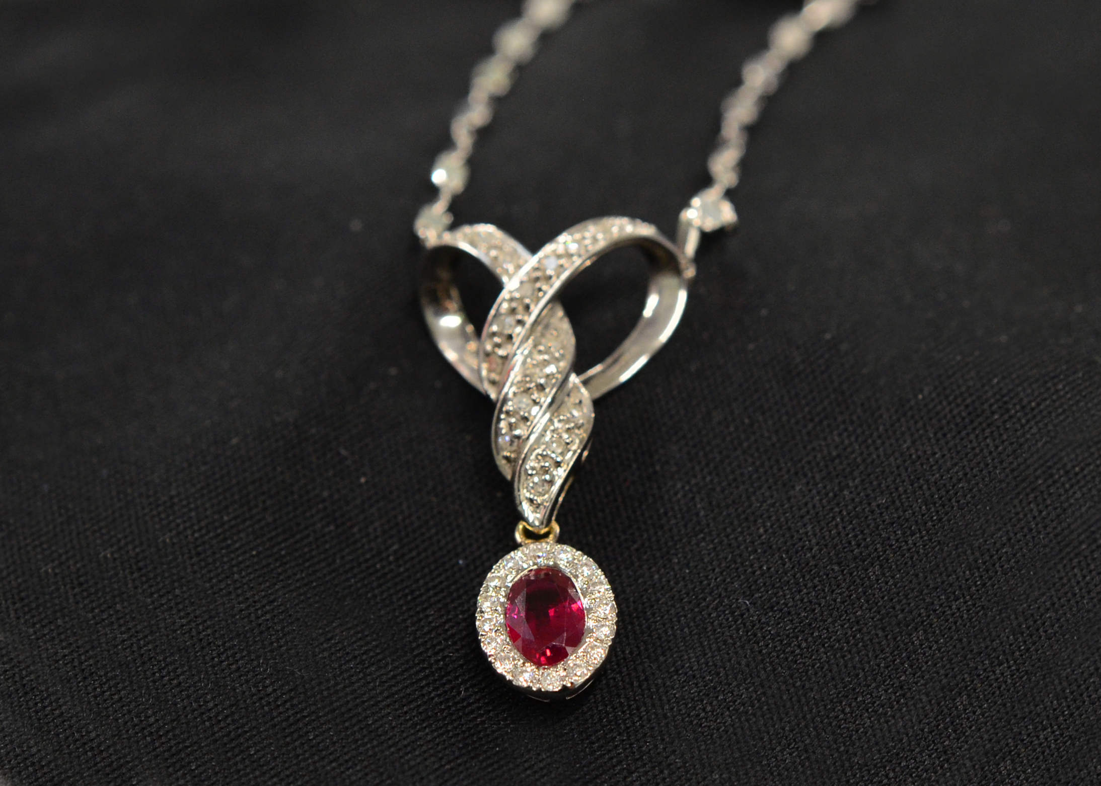 A ruby & diamond pendant H/M 14ct, suspended by a 9ct H/M chain, the oval pigeon blood red ruby