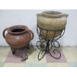 A terracotta garden urn on wrought iron stand along with one other- larger one plastic