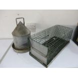 A galvanised chicken feeder along with an animal trap