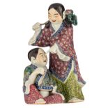 A Chinese polychrome porcelain group, depicting two playing children catching bats, the girl holding