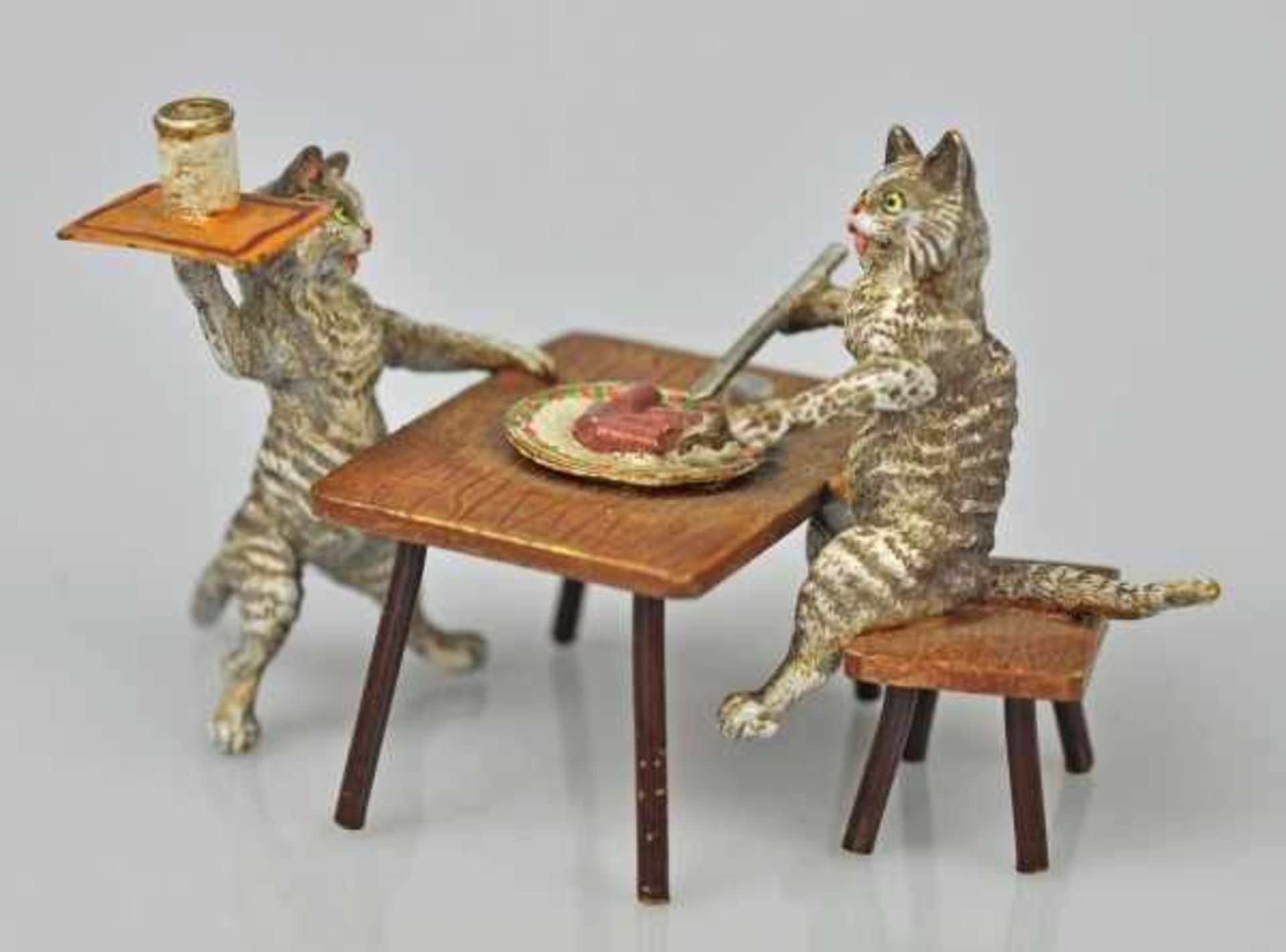 KATZENWIRTSCHAFT Katze am Tisch beim Essen, vor ihr weitere Katze als Kellner mit Tablett, Wiener