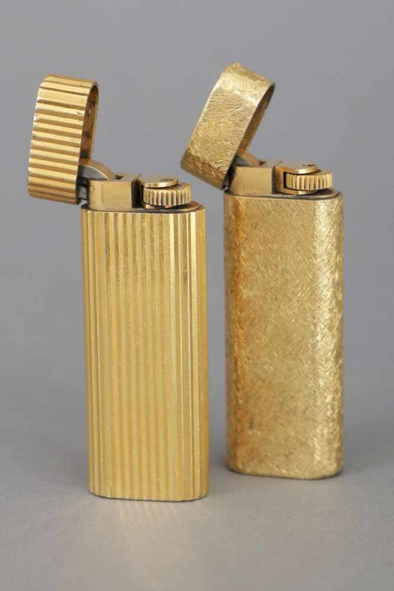 2 CARTIER Feuerzeugevergoldetes Metall, schlanke, hohe Form, gerundet, 1x Rillendekor, 1x Kerbdekor,