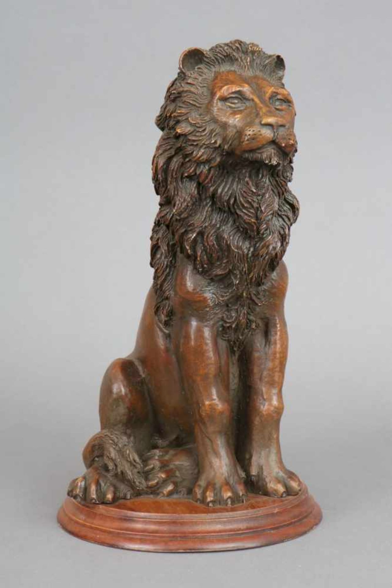 Gußfigur eines sitzenden Löwenbraun patiniert, auf rundem, profiliertem Holzsockel montiert,