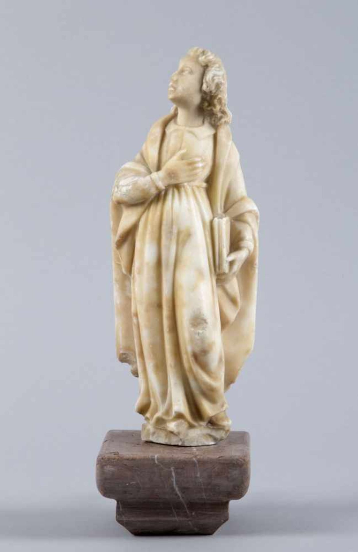 Evangelist JohannesMarmor. Standfigur mit Buch. H. 28 cm. Auf Wandkonsole aus rosa Marmor.