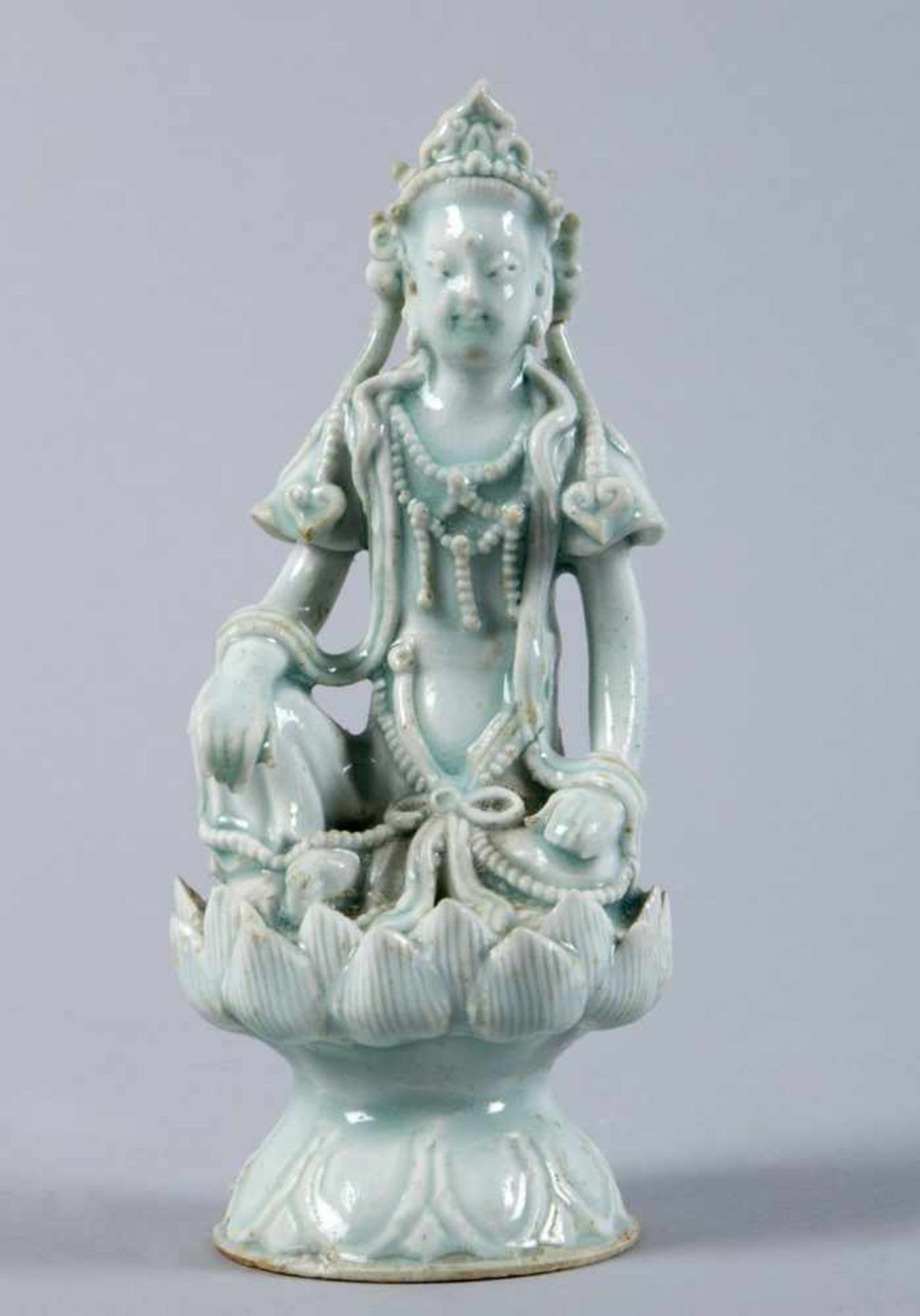 GuanyinPorzellan. Hellgrüne Glasur. Auf Lotossockel sitzend. China, wohl Qing-Dynastie. H. 16,5