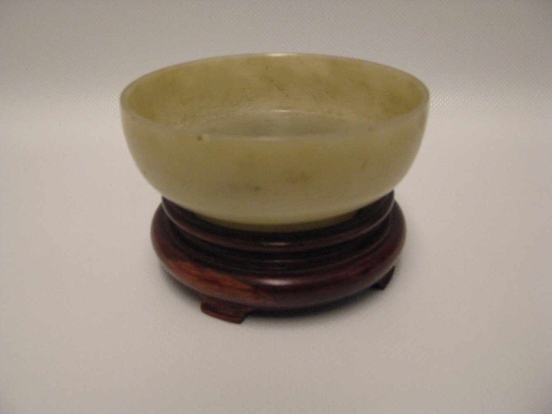Jade-Schale, China, um 1900, milchfarben-bräunliche Jade, Holzsockel, h 4 cm, d 9,5 cm.- - -19.