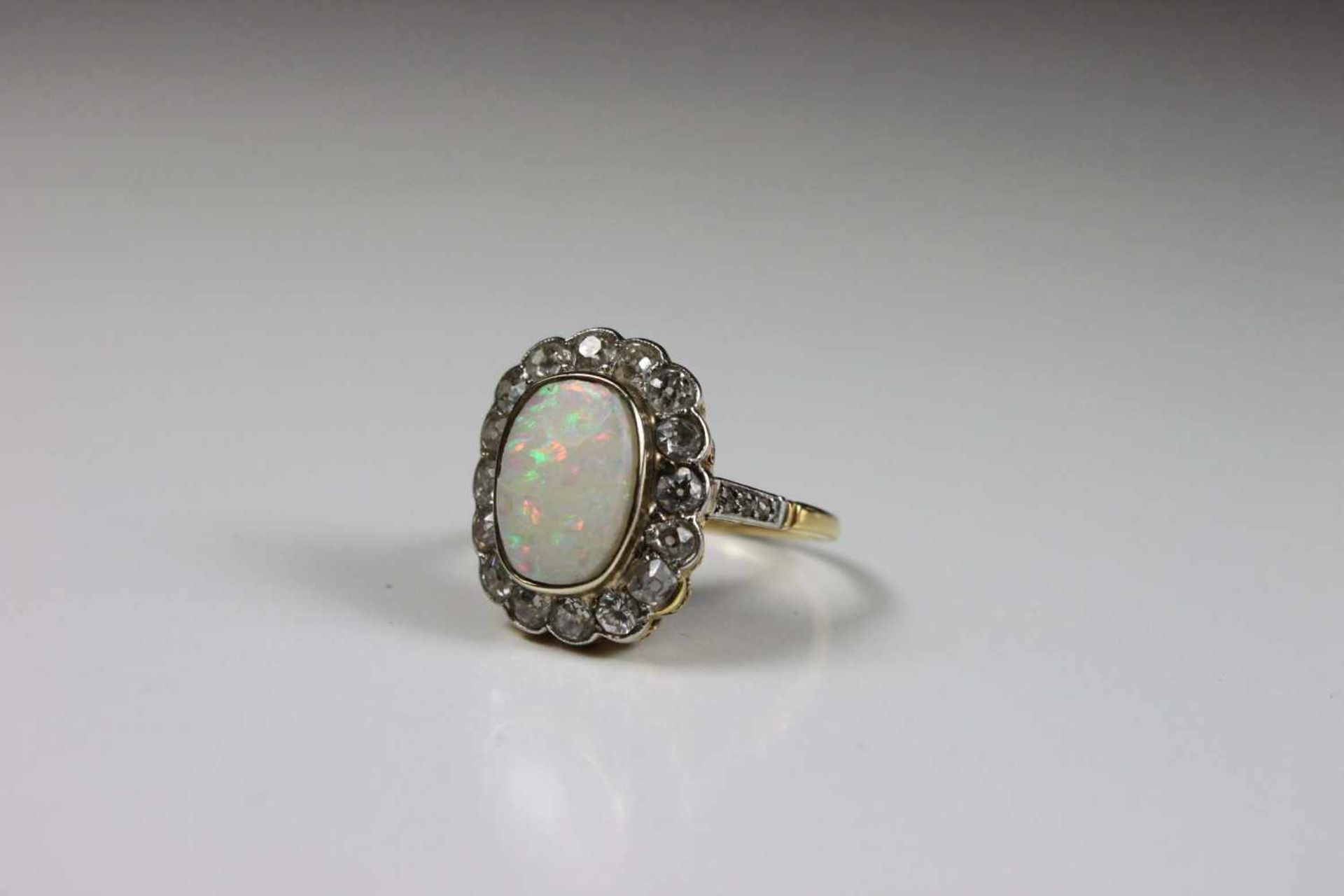 Ring, Gelbgold mit Weißgold, gefasster Opal von 16 Brillanten gerahmt, seitlich jeweils 3 weitere,