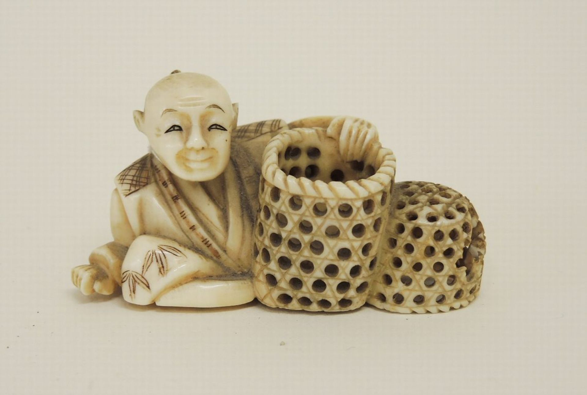 OkimonoElfenbein, fein geschnitzt. In Form eines sitzenden Mannes mit zwei Körben (kleiner Korb