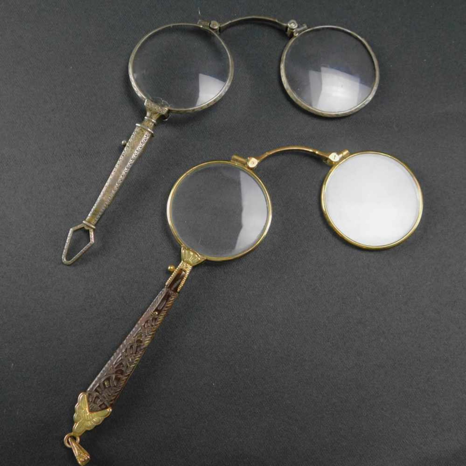 2 Longnons, aufklappbare Brillen, Anfang 20. Jhdt., Länge 11 bis 12 cmSilberfarbene Longnon: Glas am