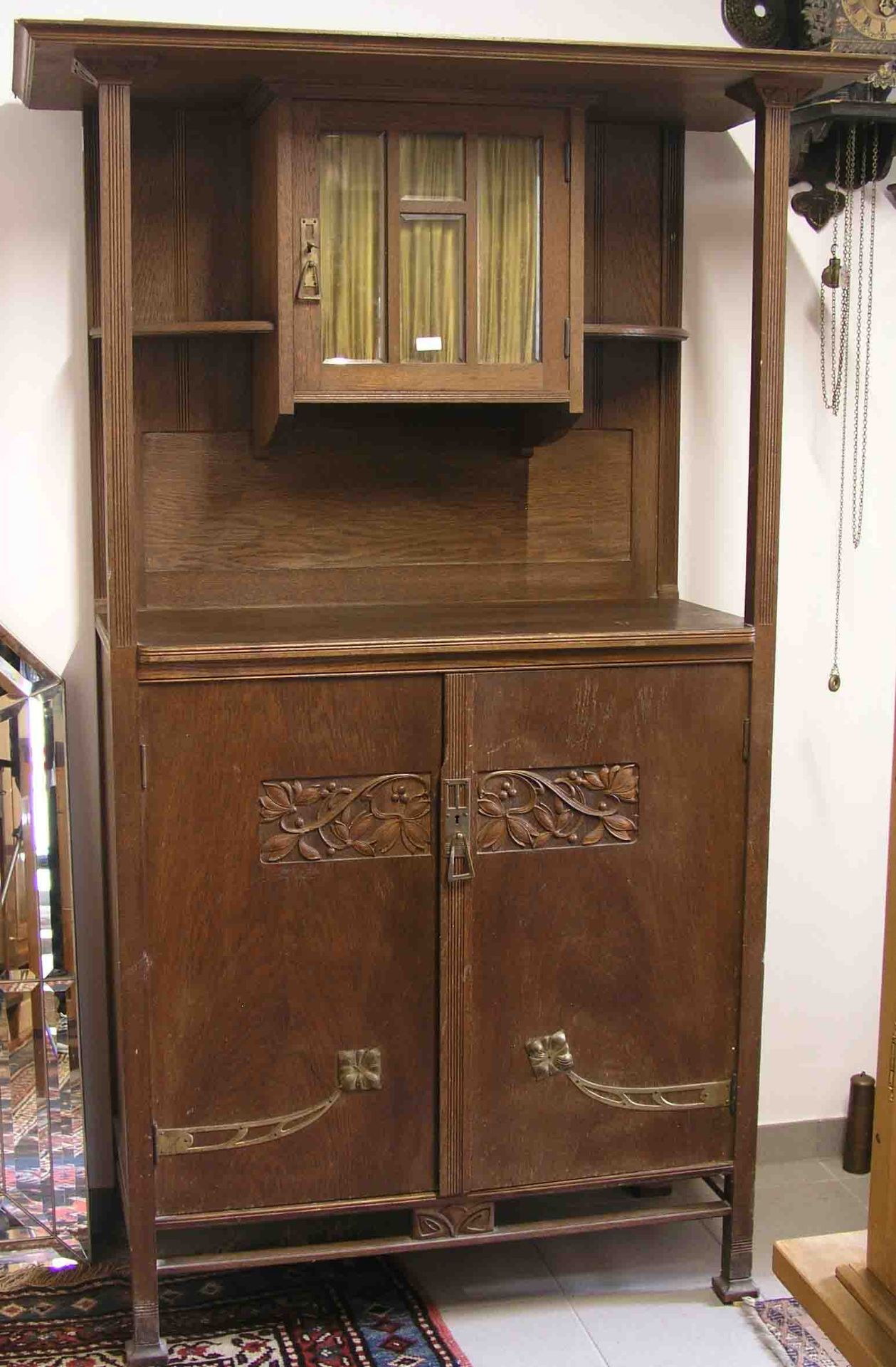 Jugendstil-Schrank. Eiche, zweittypisch beschnitzt. Zweitüriges Unterteil mitMessingbeschlägen.