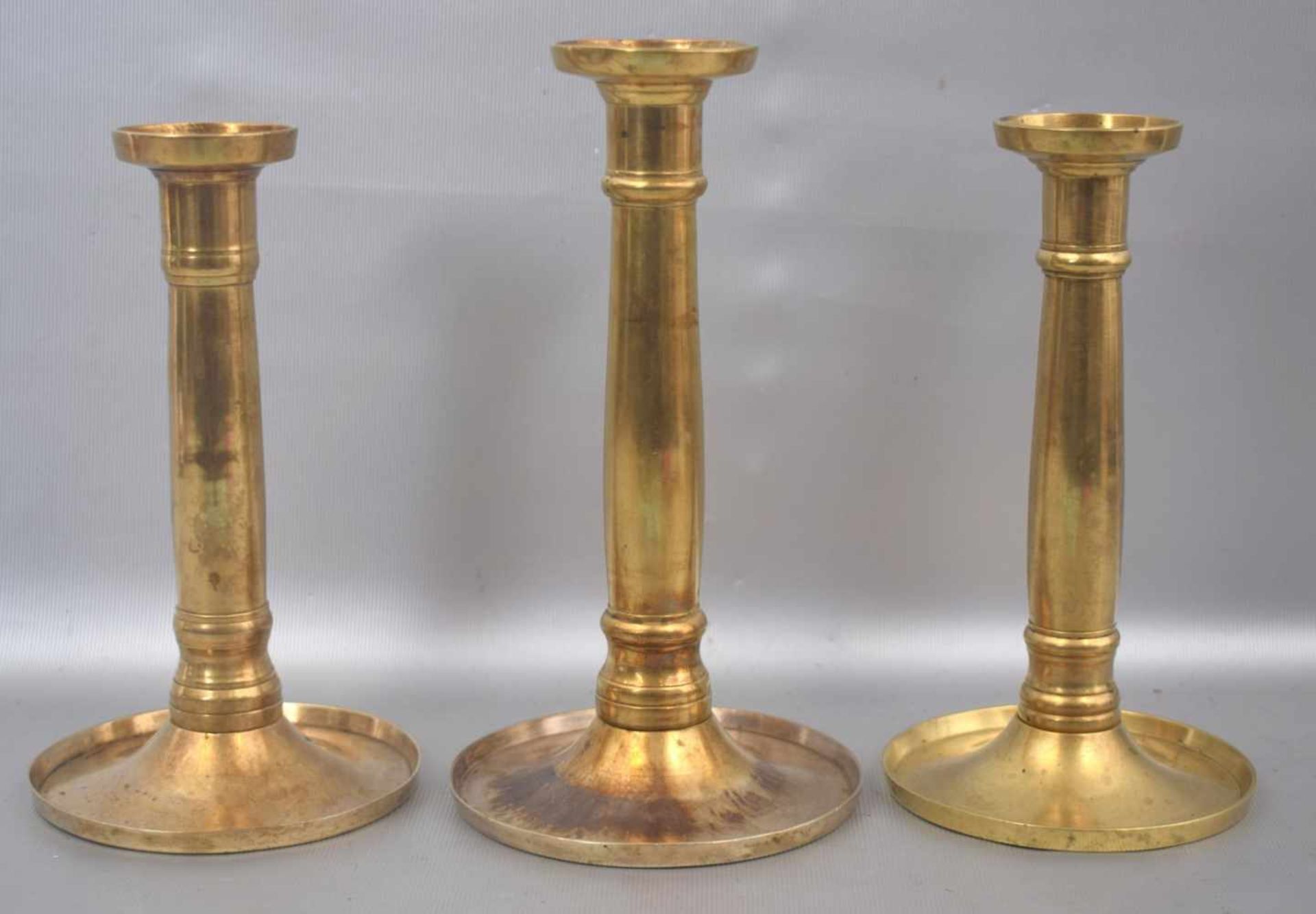 Drei Biedermeier-Kerzenleuchter1-lichtig, Messing, runder Fuß und Schaft, H 21 cm bzw. 19. cm, 1.