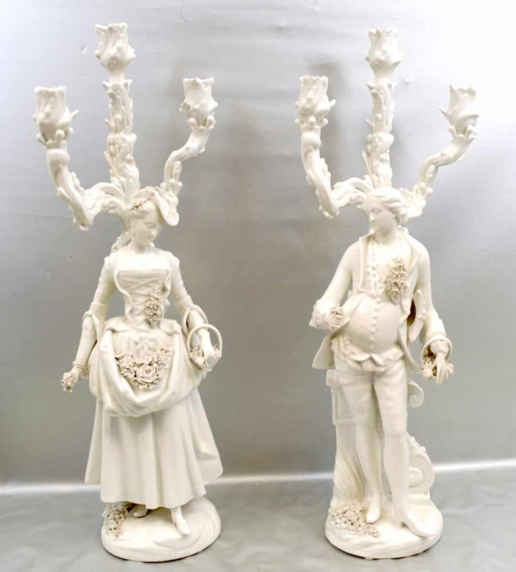 Paar Prunk-Kerzenleuchterje 3-lichtig, weiß glasiert, auf rundem Sockel stehend, figürliche