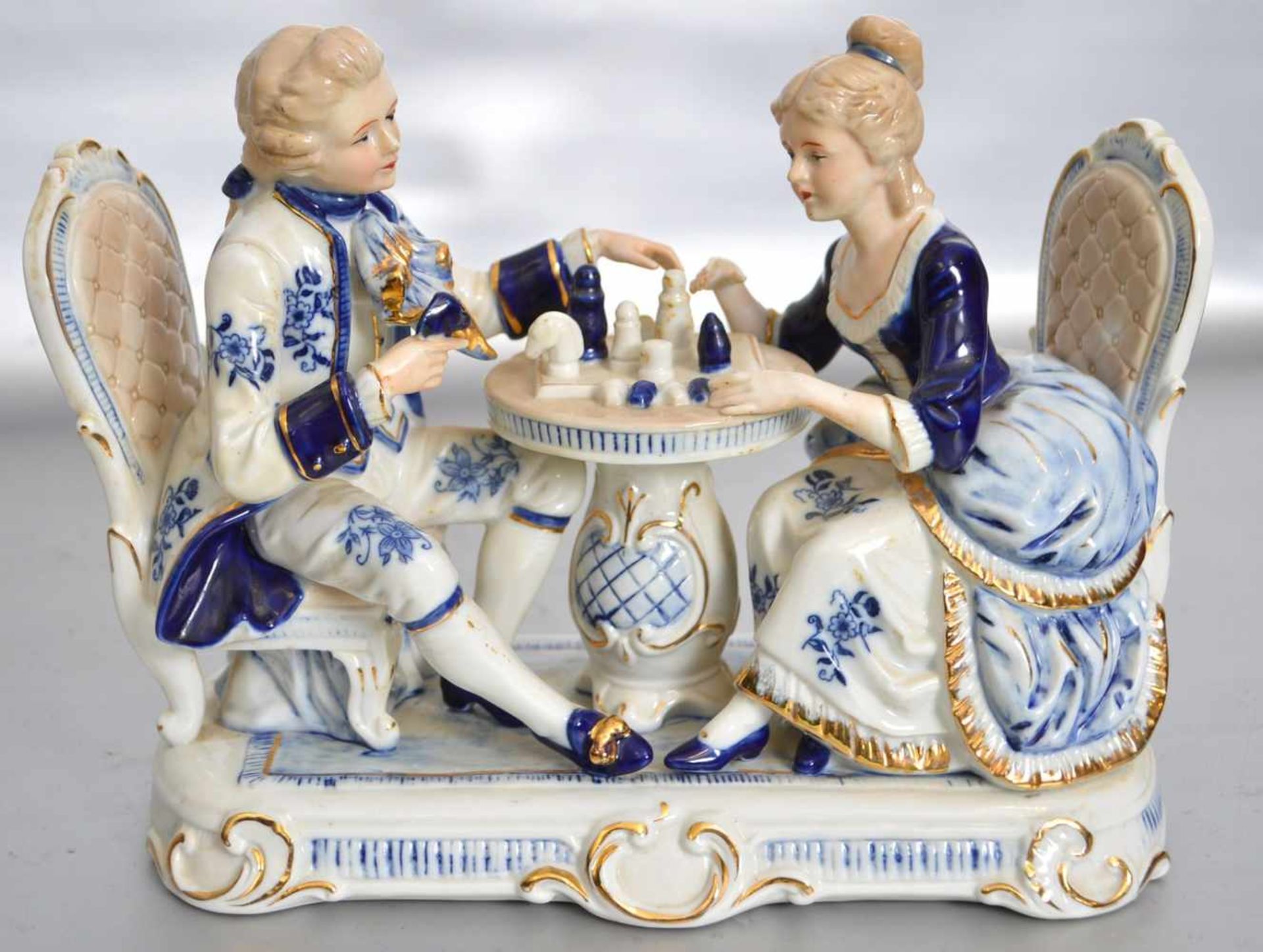 FigurenpaarElegantes Paar am Tisch sitzend, auf rechteckigem Sockel, blau/gold bemalt, H 21 cm, B 27