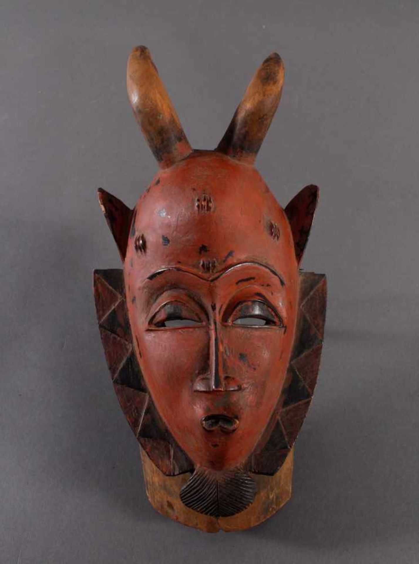 Maske der Baule, ElfenbeinküsteHolz geschnitzt, rot-schwarz gefärbt, Narbentatauierungen, mit