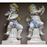 A pair of decorative ceramic cherubs, playing musical instruments, scantily clad,