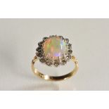 An opal and diamond cluster ring, central oval opal cabochon, flashing red,