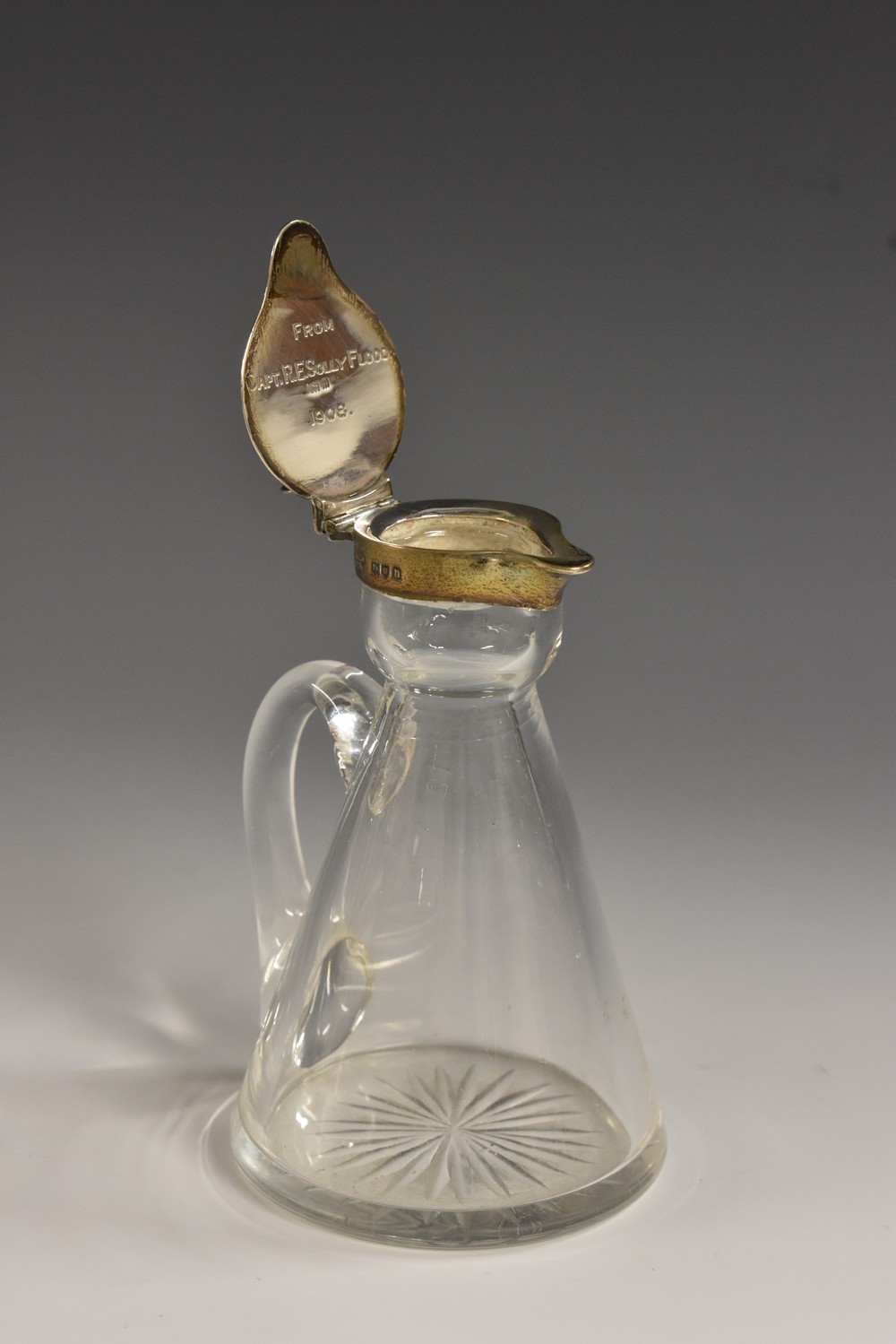 An Edwardian silver mounted clear glass whisky noggin, hinged cover, scroll handle, star-cut base,