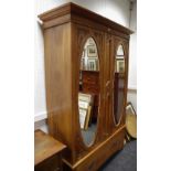 An Art Nouveau double wardrobe outswept cornice two oval mirrored doors brass loop handles deep