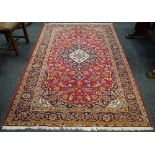 A Kashan rug, floral designs in hues of cornflower blue, indigo, pink and yellow on a red ground.