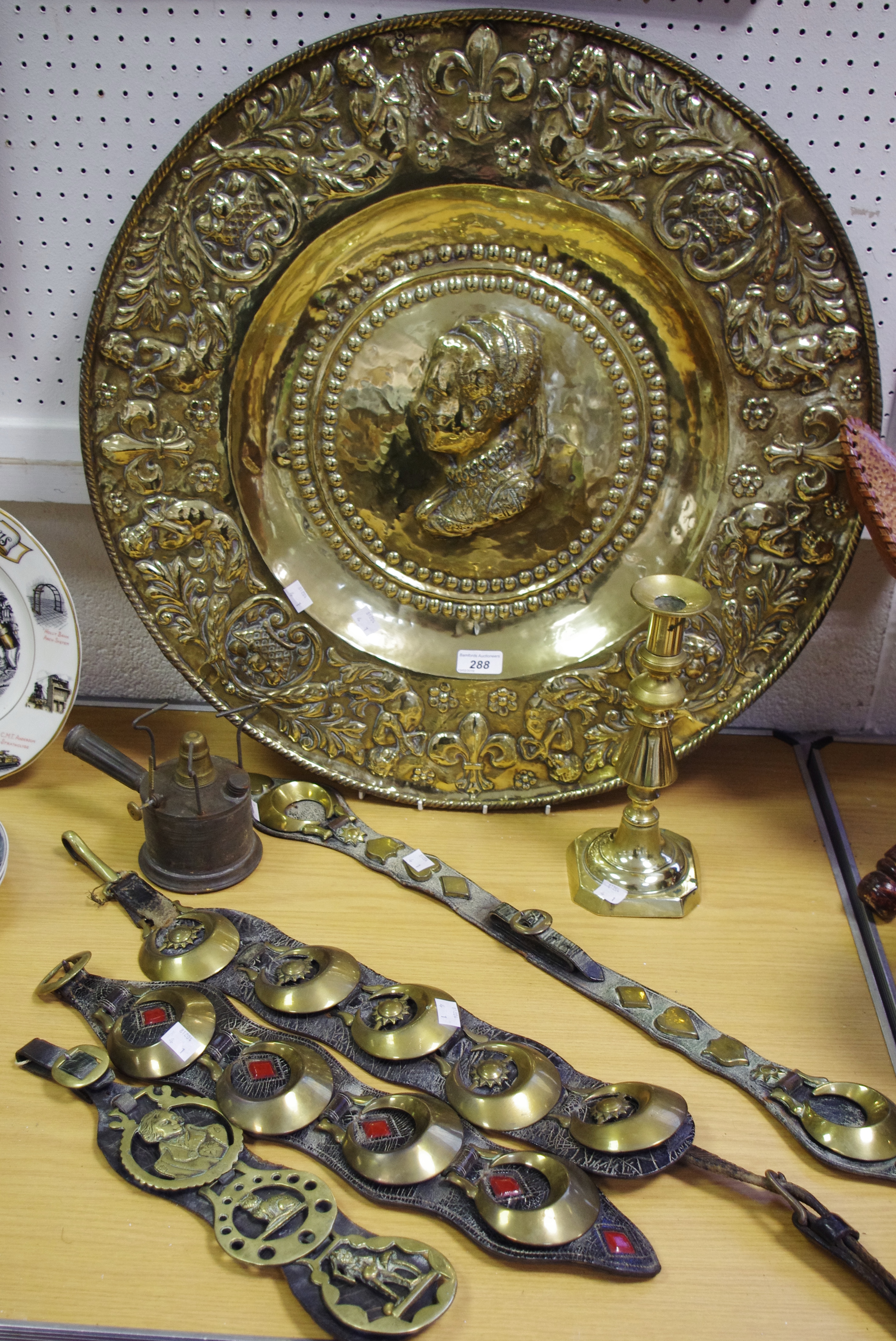 A large embossed brass charger; horse brasses; an ejector candlestick;