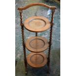 An early 20th century oak three tier cake stand, shaped carry handle above three dished stands,