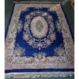 A Chinese woollen carpet, in tones of blush and green on a deep blue ground,