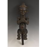 Tribal Art - a Baule spirit spouse figure, modelled seated, holding a vessel, 44cm long,