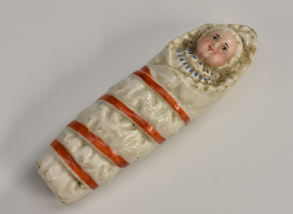 A 19th century German porcelain novelty whistle, as a swaddled baby, 7.5cm long, c.