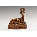 A late 19th century treacle-glazed stoneware model, of a recumbent stag, on a grassy ground, 14.