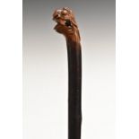 A novelty softwood walking stick, the carved grotesque mask grip enclosing a 'puzzle' ball,