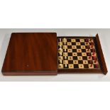 An early 20th century mahogany travelling chess set, the sliding cover enclosing bone pieces,