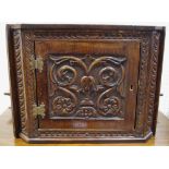 An early 20th century oak splay fronted cabinet, the doors carved with scrolling foliage, 30cm high,