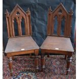 A pair of Gothic Revival oak hall chairs, architectural pierced and carved backs, boarded seat,
