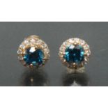 A pair of blue and white diamond earrings, each with a central blue round brilliant cut diamond,