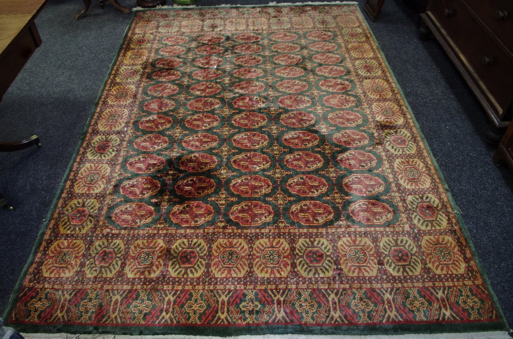 A woollen rug, decorated with geometric motifs in red and cream on green ground. 275cm x 184cm.