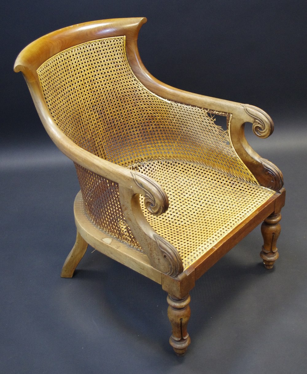 A Regency mahogany bergere elbow chair, curved top rail, outswept arms, scrolling terminals,