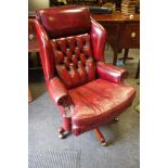 An Ox blood leather wing back office swivel chair, button back scrolling arms squab cushion.