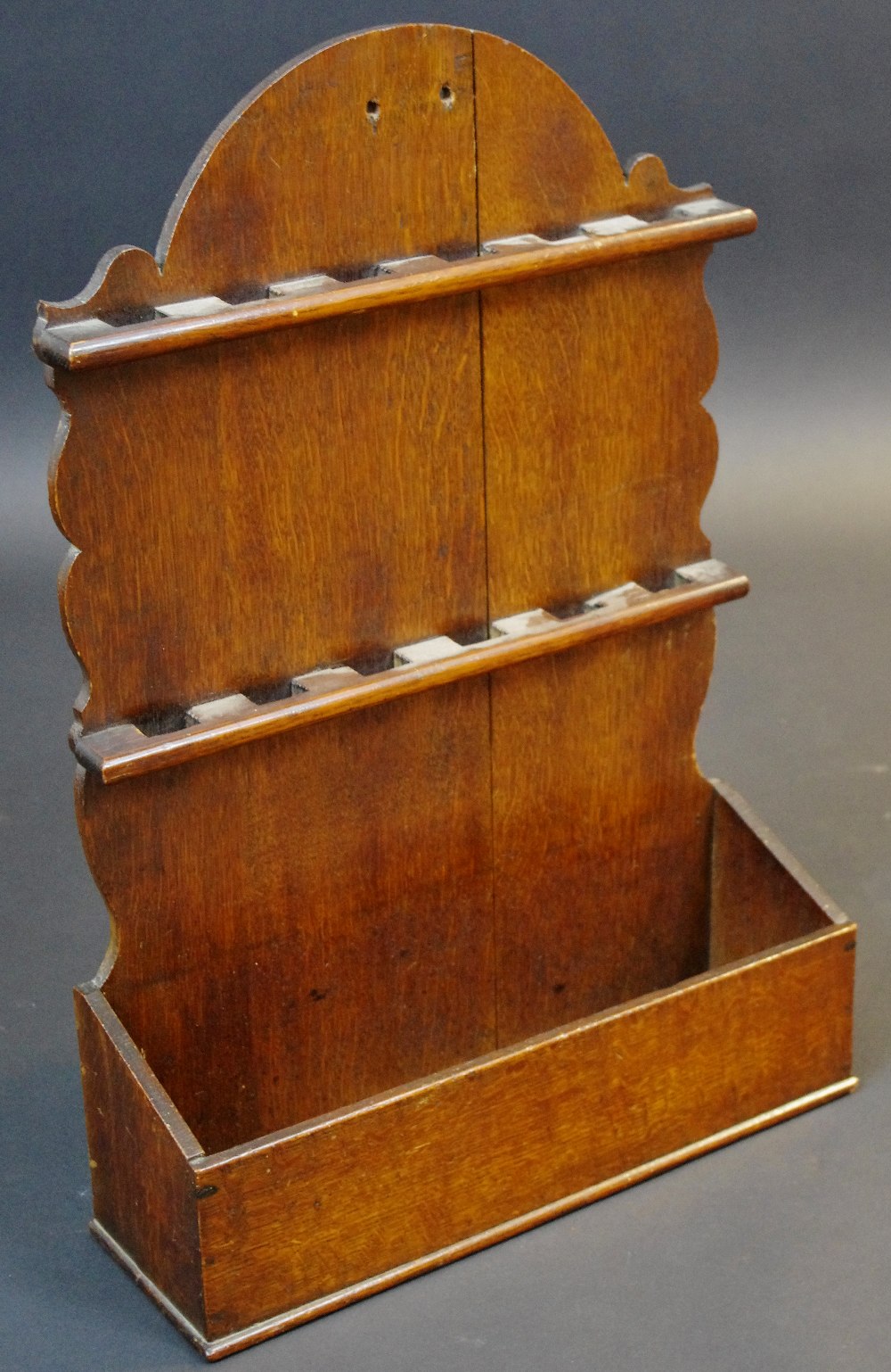 A 19th century oak spoon rack, arched cresting above two rows of apertures, candle well to base,