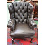 A Chesterfield type wingback armchair, deep buttoned upholstery, scroll arms,