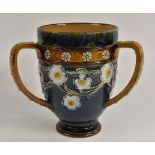 A Doulton Lambeth stoneware three handled tyg, tube lined with a band of white and blue flowers,