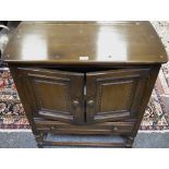 A dark oak side cupboard, oversailing top, two fielded panel doors over long drawer, turned legs.