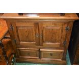 An oak side/media cabinet, rectangular top above a pair of panel doors and two short drawers,