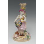 A Minton figural candlestick, with a girl in colourful dress, holding a basket of flowers,