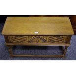 An oak long stool, hinged seat opening to storage, carved panel front, turned and blocked legs.