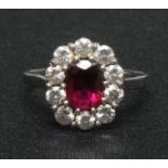 An 18ct white gold ruby and diamond cluster ring, the central faceted ruby of good colour,