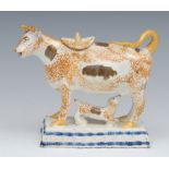 A Prattware cow creamer and cover, standing four square, sponged in ochre, tan patch markings,