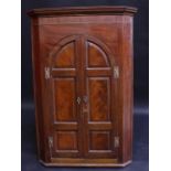 A George III mahogany corner cabinet, stepped cornice, two arched panelled doors, 138cm high,