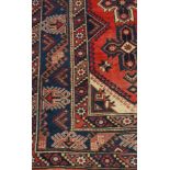 A Persian woollen rug, with three geometrical motifs, banded geometrical borders, in red,